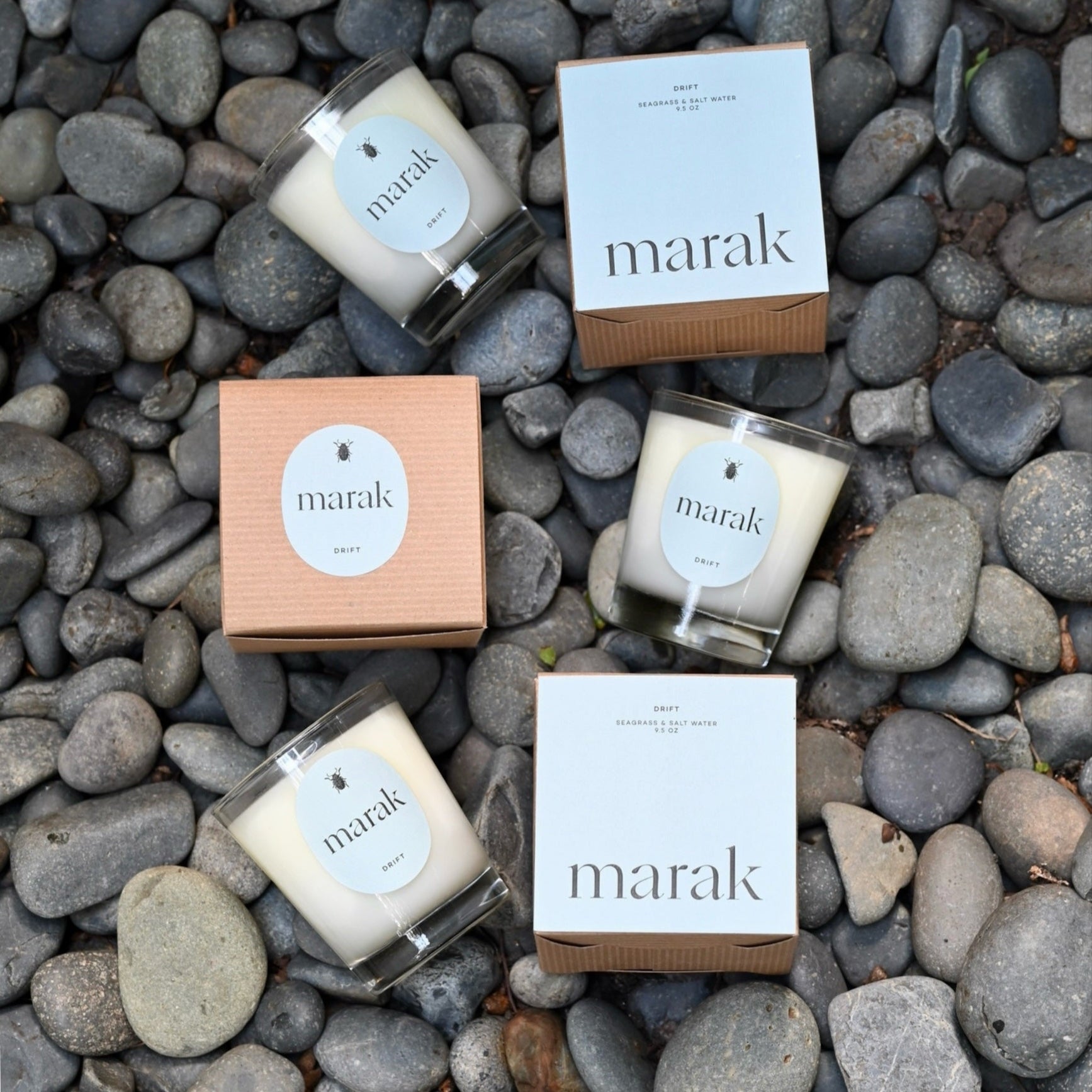 Four 'marak' candles and boxes arranged on a bed of gray stones.