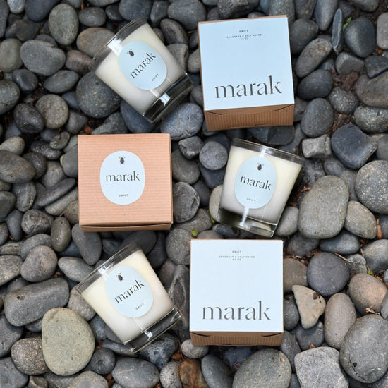 Four 'marak' candles and boxes arranged on a bed of gray stones.